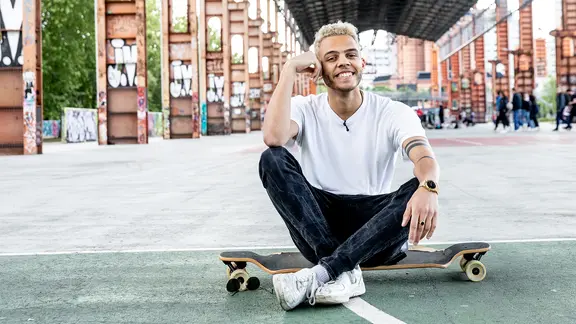 Malik Harris sitzt lachend auf einem Skateboard in Turin.