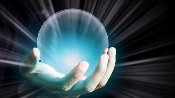 Eine leuchtende Glaskugel wird vor dunklem Hintergrund gehalten.