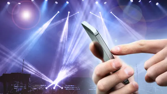 Hand tippt auf einem Smartphone vor einer Bühnenszene. (Montage)