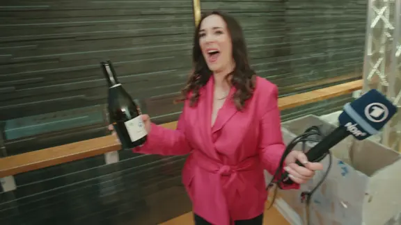 Alina Stiegler mit einer Flasche Sekt und einem NDR Mikrofon in der Hand.